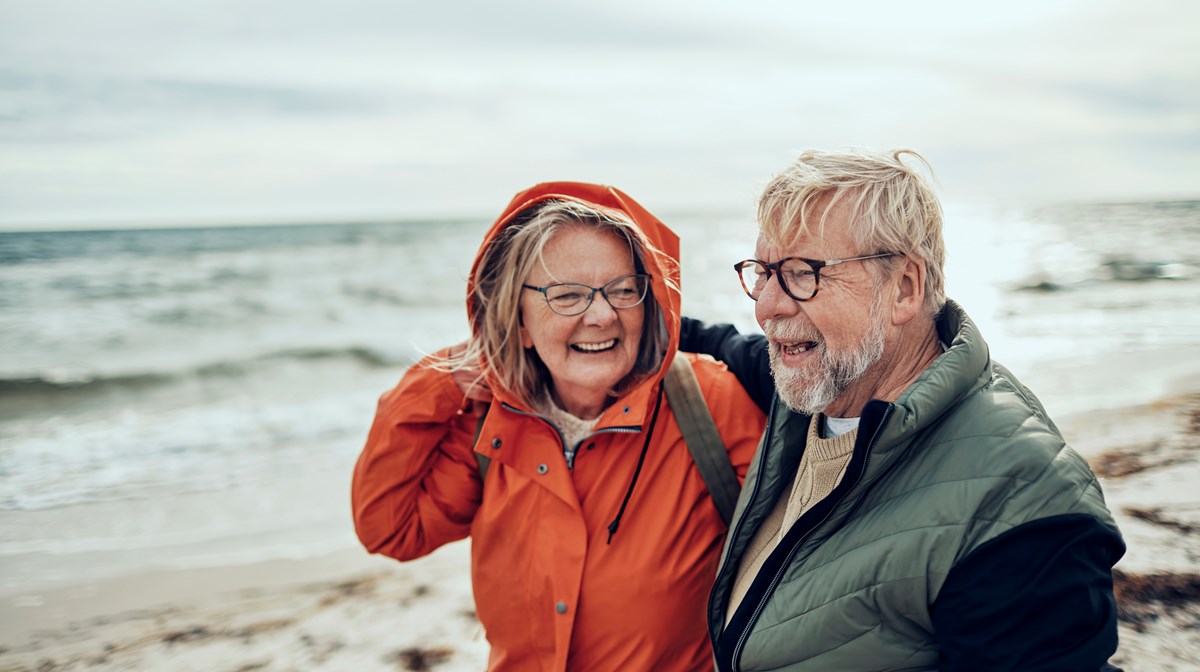 Äldre kvinna och äldre man går på stranden