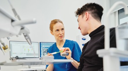 Kvinnlig tandhygienist på Folktandvården förklarar fördelarna med Frisktandvård för en yngre manlig patient. 