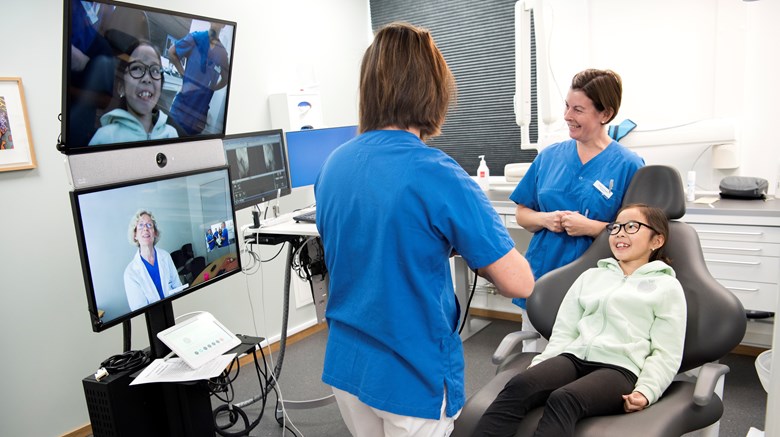 En tandläklare och en tandsköterska undersöker en patient samtidigt som de har kontakt med en specialisttandläkare via en videoutrustning.