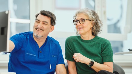 Manlig tandläkare hos Folktandvården förklarar vad Frisktandvård kostar för en kvinnlig patient som sitter bredvid i en behandlingsstol.